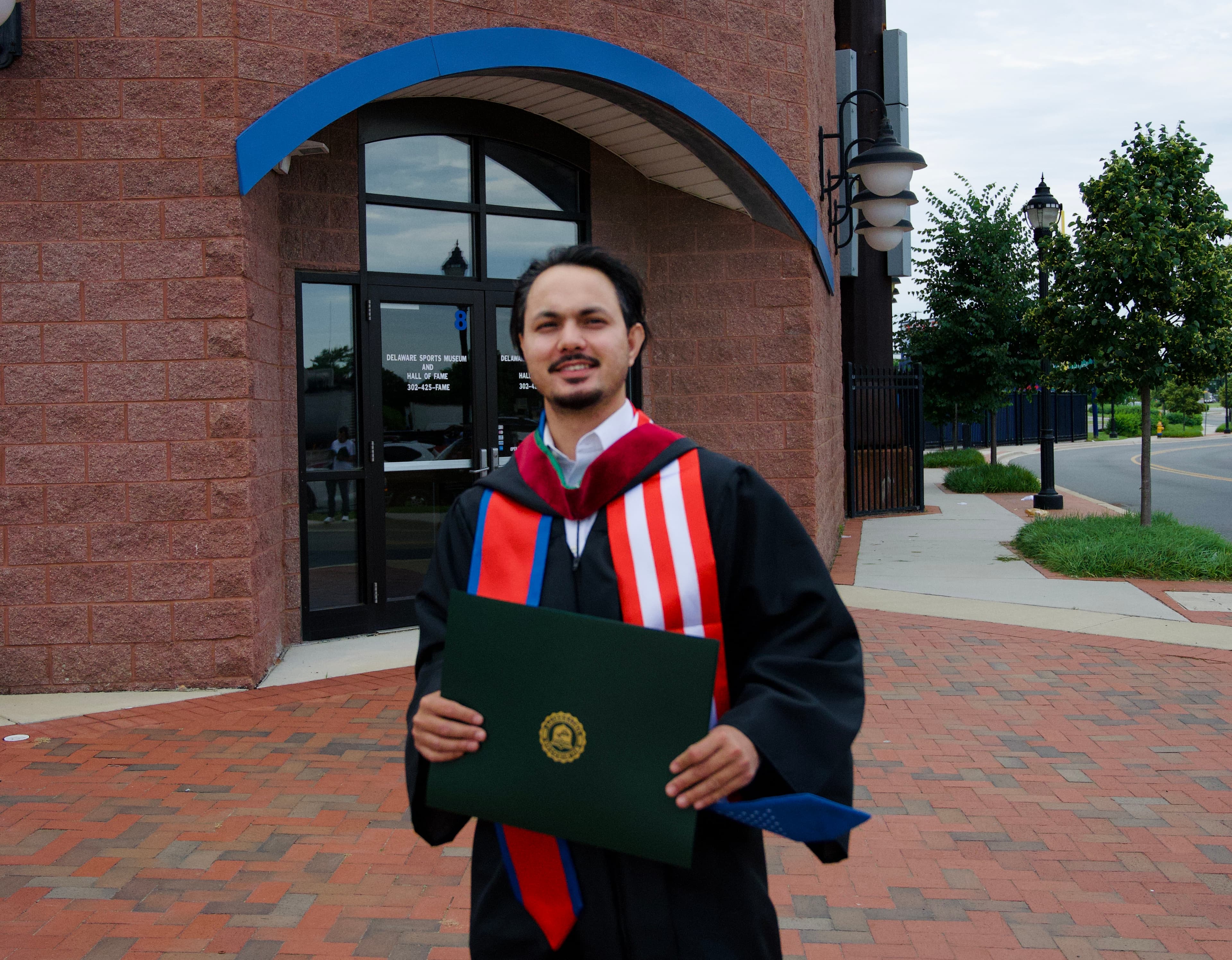 Rajesh wearing academic regalia and holding his diploma at graduation